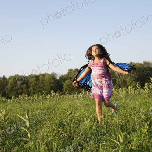 A young girl running across a field, wearing fabric butterfly wings. A young girl running across a field, wearing fabric butterfly wings.