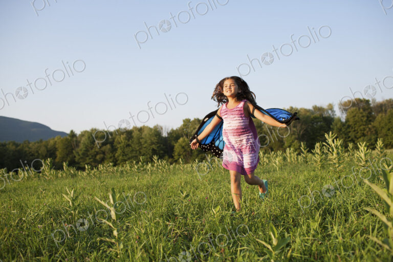 A young girl running across a field, wearing fabric butterfly wings.