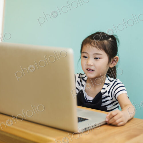 A young girl seated at a laptop computer in a classroom.