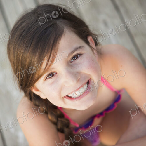 A young girl seated on a jetty looking upwards.