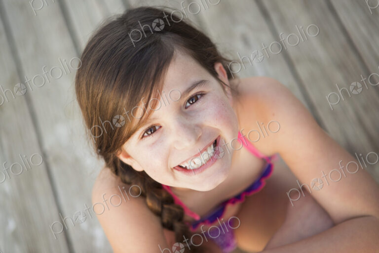 A young girl seated on a jetty looking upwards.