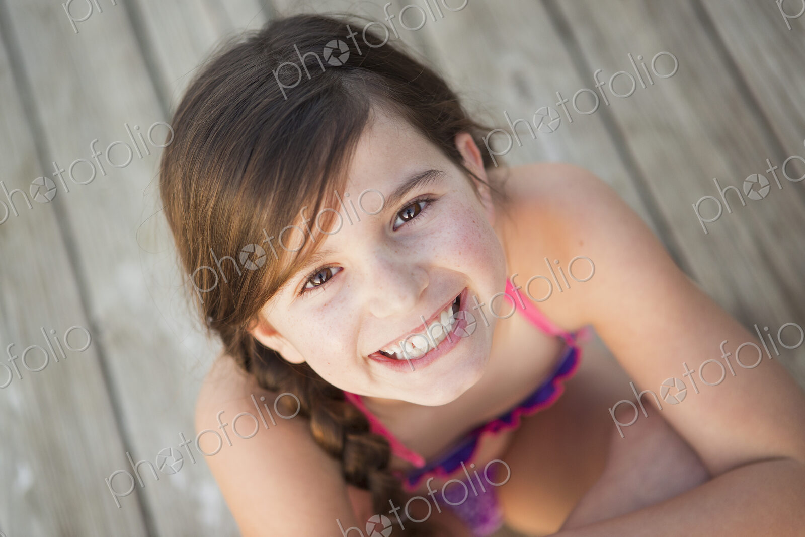 A young girl seated on a jetty looking upwards.