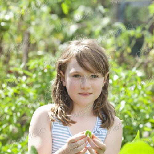 A young girl sitting among the fresh green foliage of a garden. A young girl sitting among the fresh green foliage of a garden.