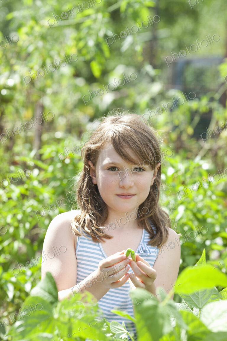 A young girl sitting among the fresh green foliage of a garden.