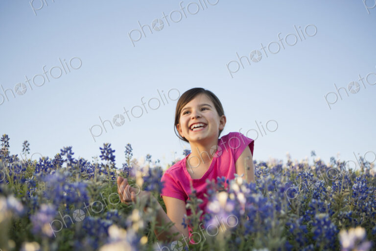 A young girl sitting in a field of wild flowers, laughing.