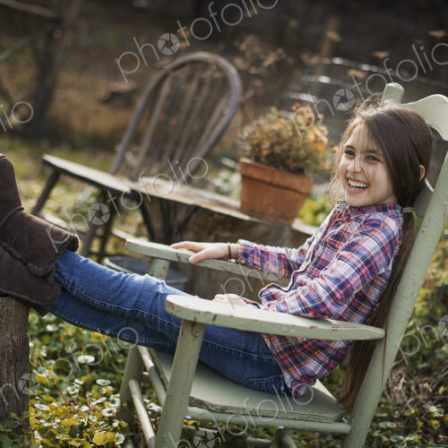 A young girl sitting in a wooden chair in a garden, with her feet up on a log. A young girl sitting in a wooden chair in a garden, with her feet up on a log.