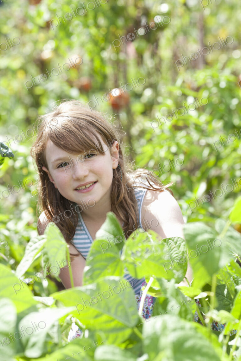 A young girl sitting in among the fresh green foliage of a garden. Vegetables and…