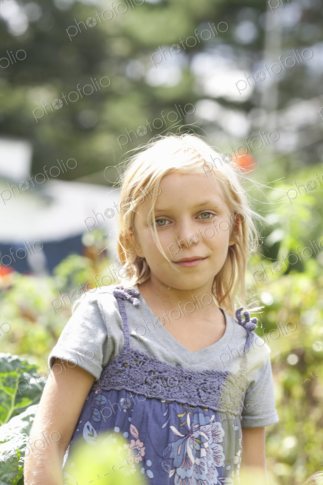 A young girl sitting in among the fresh green foliage of a garden. Vegetables and…
