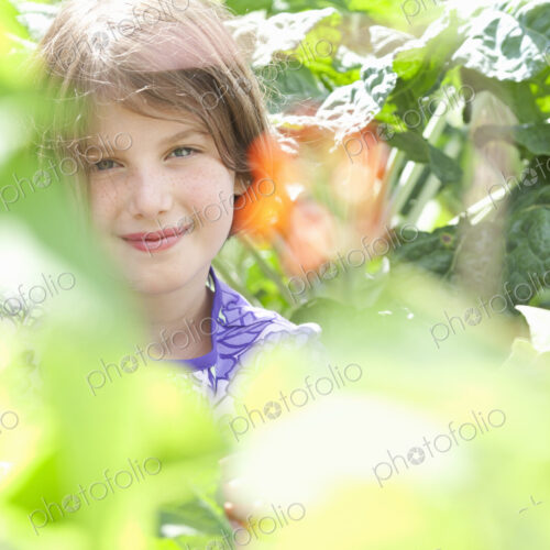 A young girl sitting in among the fresh green foliage of a garden. Vegetables and… A young girl sitting in among the fresh green foliage of a garden. Vegetables and…