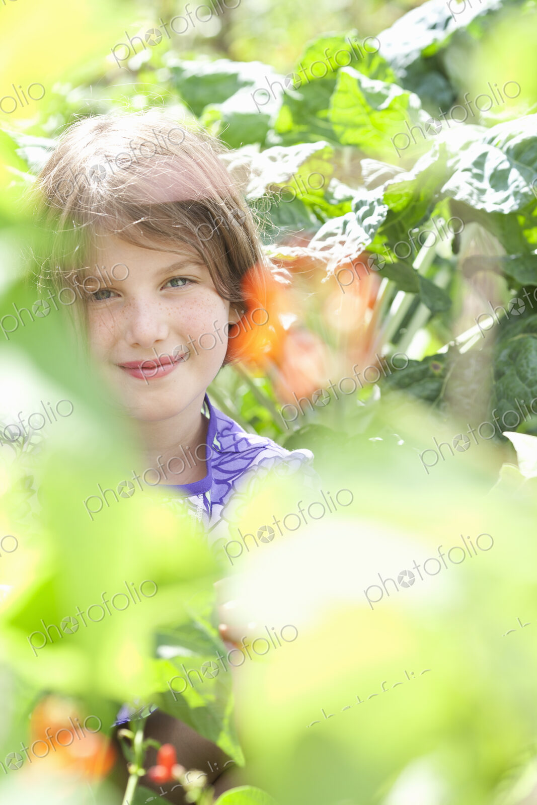A young girl sitting in among the fresh green foliage of a garden. Vegetables and…