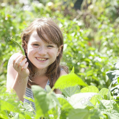 A young girl sitting in among the fresh green foliage of a garden. Vegetables and… A young girl sitting in among the fresh green foliage of a garden. Vegetables and…
