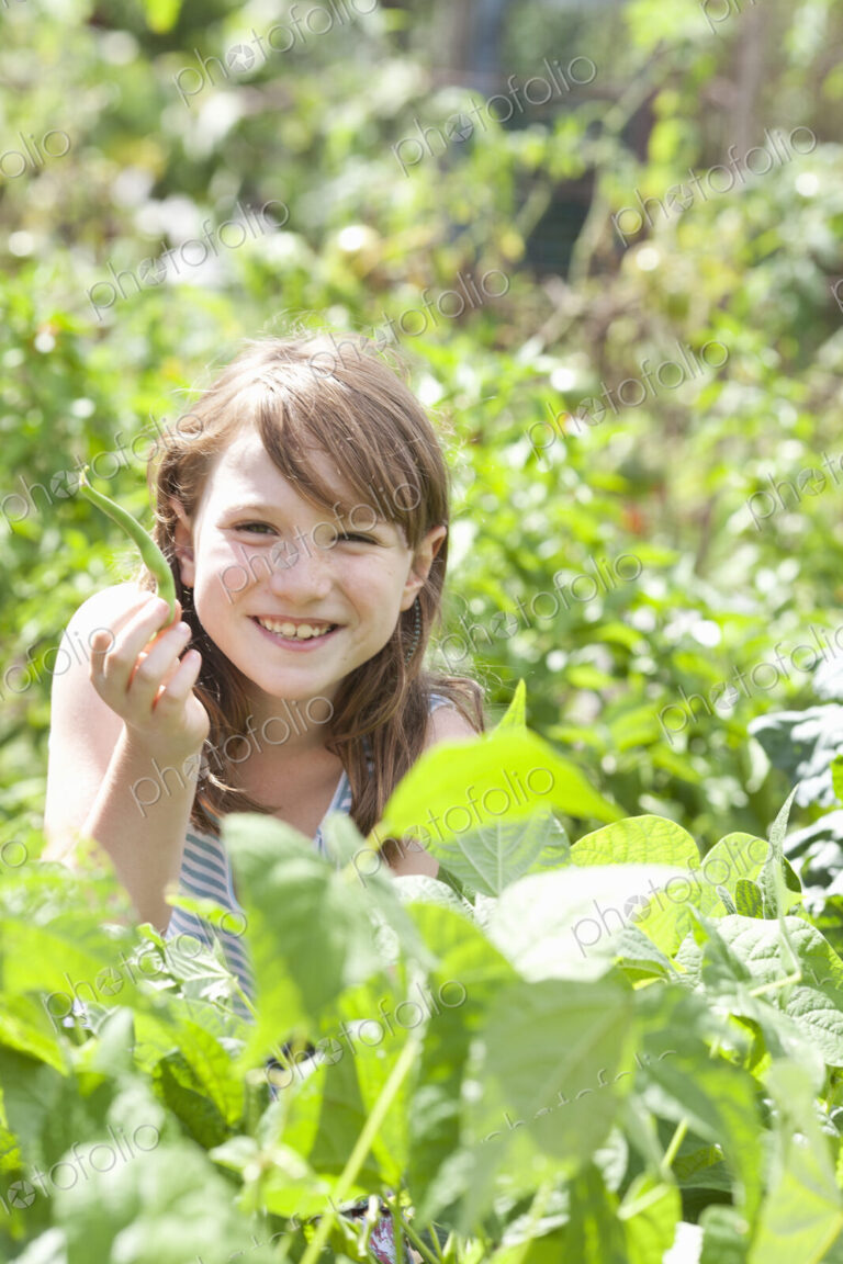 A young girl sitting in among the fresh green foliage of a garden. Vegetables and…