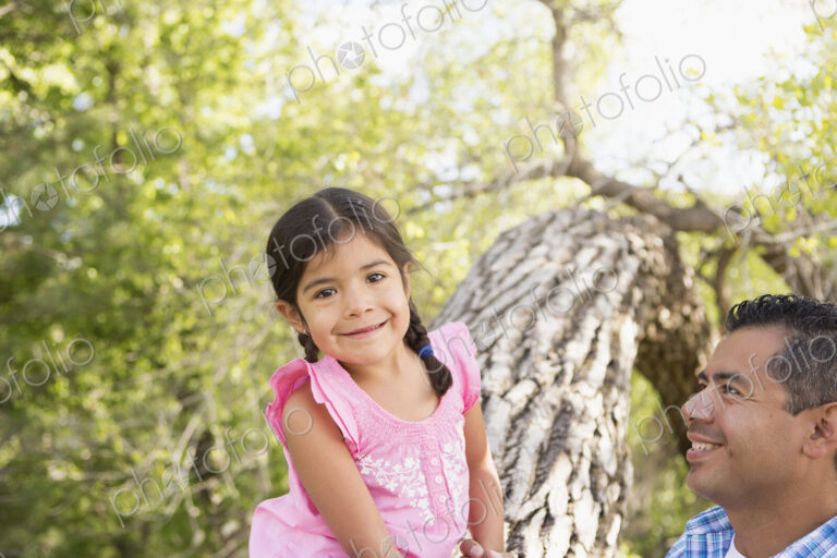 A young girl sitting on a tree trunk beside her father.