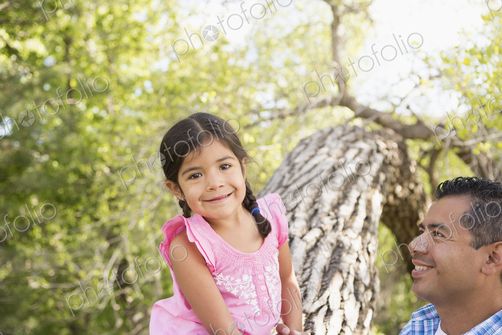 A young girl sitting on a tree trunk beside her father.