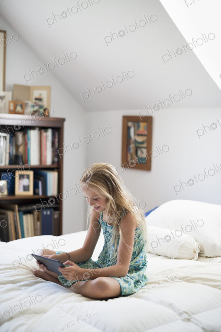 A young girl sitting on her bed using a digital tablet.