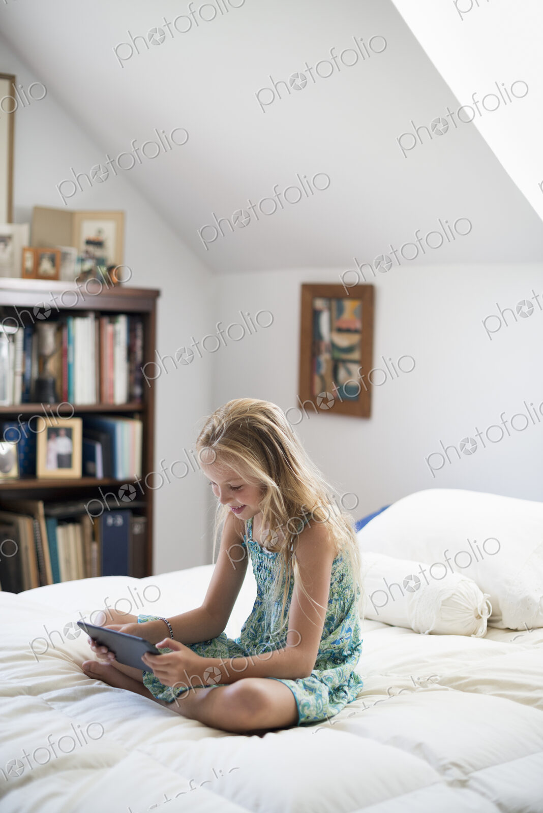A young girl sitting on her bed using a digital tablet.