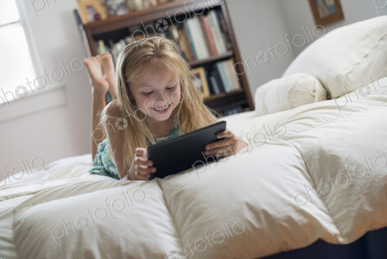 A young girl sitting on her bed using a digital tablet.