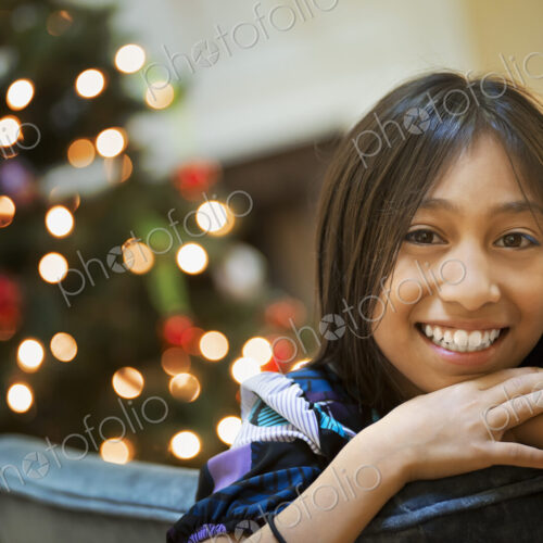 A young girl smiling and leaning over a chairback, in front of a Christmas tree. A young girl smiling and leaning over a chairback, in front of a Christmas tree.