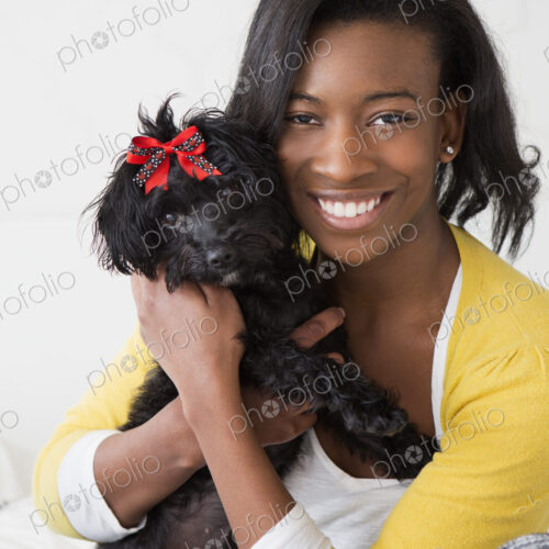 A young girl smiling, holding her small black pet dog.