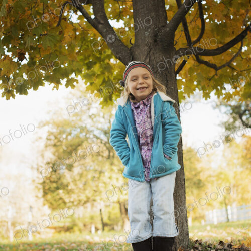 A young girl standing under a tree, on a farm. Autumn foliage.