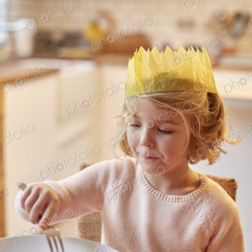 A young girl wearing a party hat, sitting at a table having a meal.