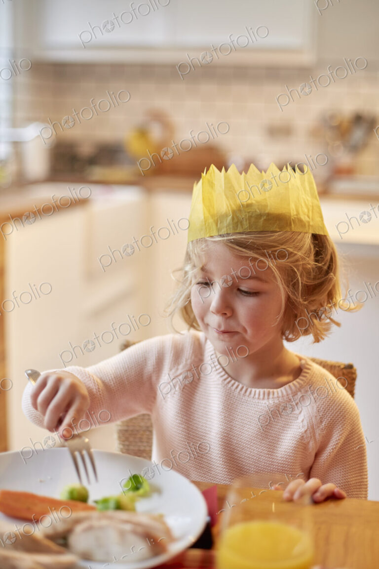 A young girl wearing a party hat, sitting at a table having a meal.