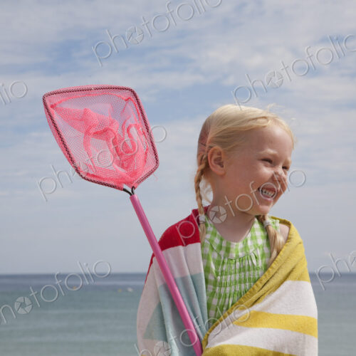 A young girl with a beach towel around her shoulders, carrying a small fishing net. A young girl with a beach towel around her shoulders, carrying a small fishing net.
