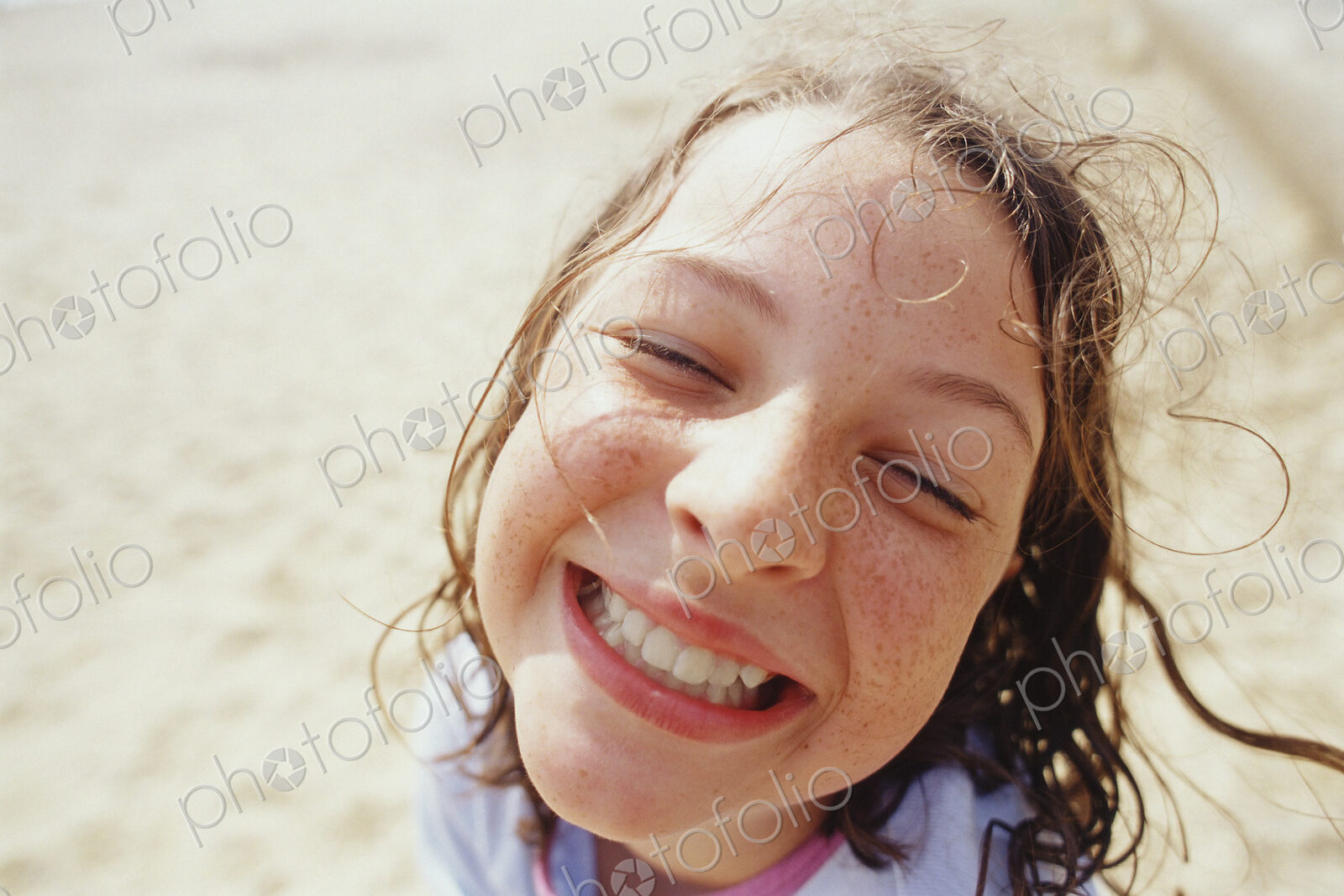 A young girl with a wide grin, eyes half closed, and wet hair outside in the rain.
