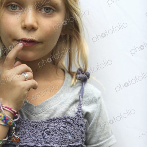 A young girl with blonde hair, and blue eyes. Her hand to her mouth. A young girl with blonde hair, and blue eyes. Her hand to her mouth.