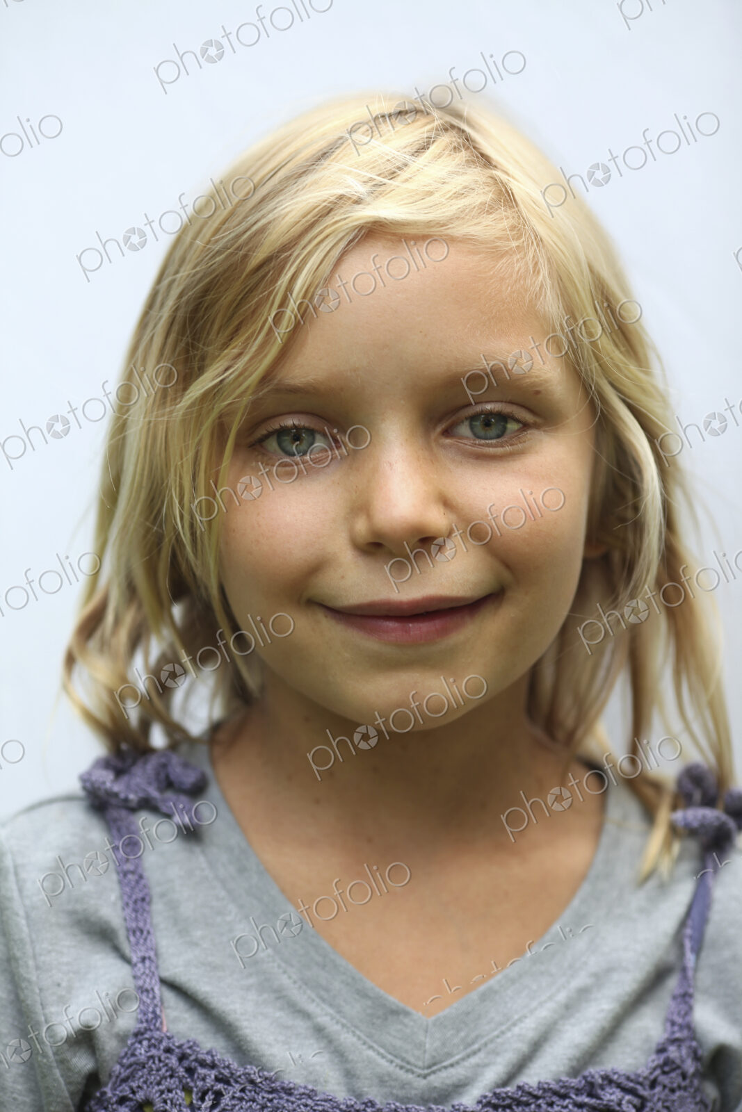 A young girl with blonde hair, and blue eyes. Smiling and looking at the camera.