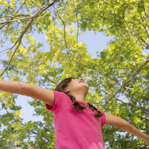 A young girl with braids wearing a pink top with her arms outstretched and head back. A young girl with braids wearing a pink top with her arms outstretched and head back.