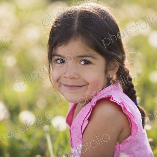 A young girl with brown hair and braids, in a wild flower meadow.