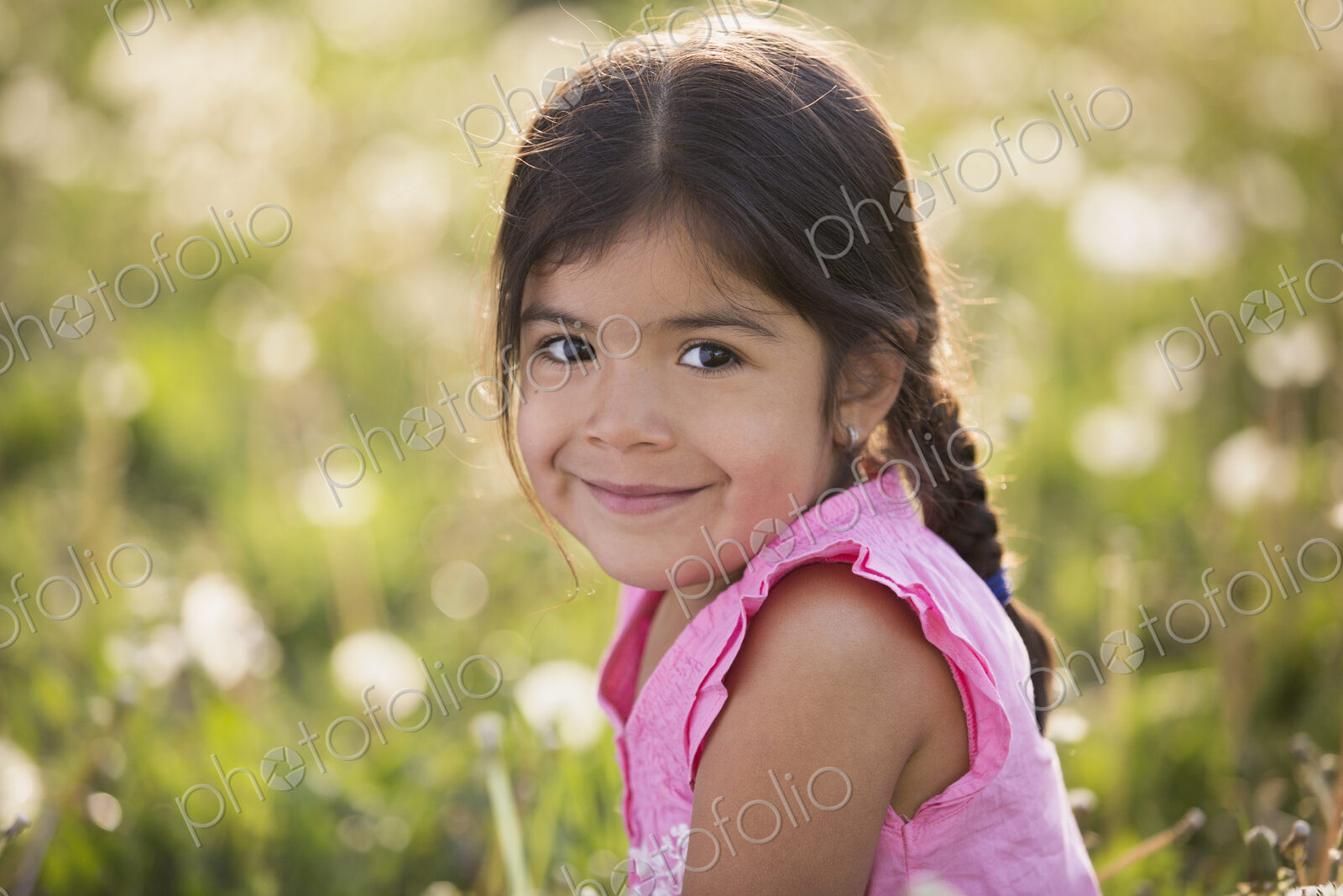 A young girl with brown hair and braids, in a wild flower meadow.