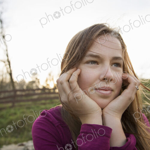 A young girl with her chin in her hands, leaning on a fence at an animal sanctuary.