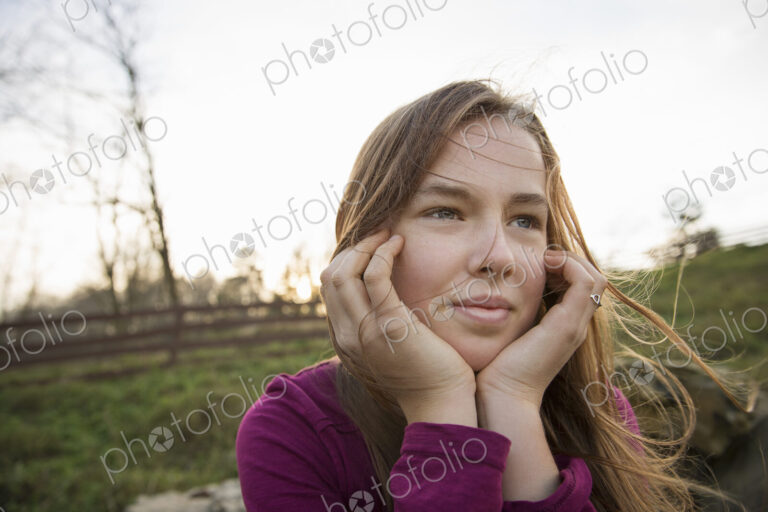 A young girl with her chin in her hands, leaning on a fence at an animal sanctuary.