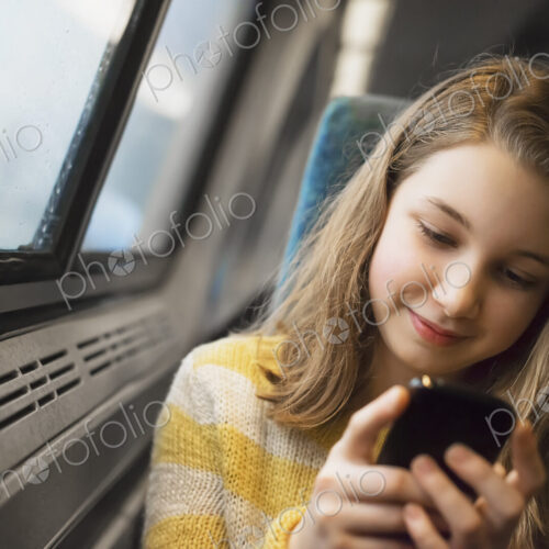 A young girl with long blonde hair sitting by a window on a train, using her mobile… A young girl with long blonde hair sitting by a window on a train, using her mobile…