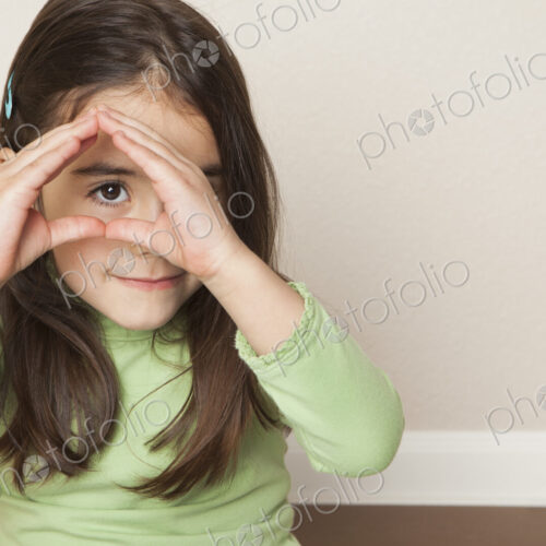 A young girl with long brown hair holding her hands up to her face, and peeping…