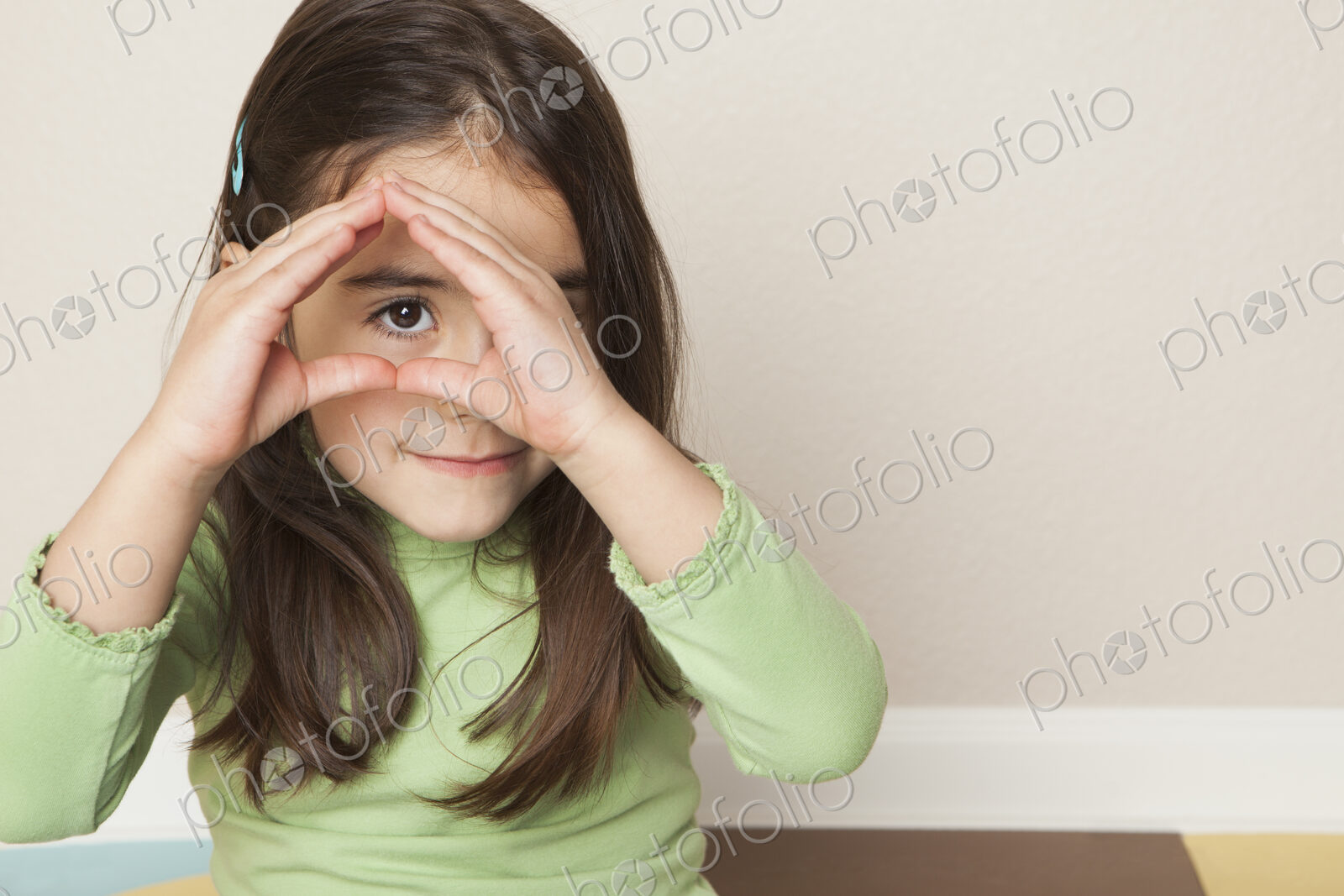 A young girl with long brown hair holding her hands up to her face, and peeping…