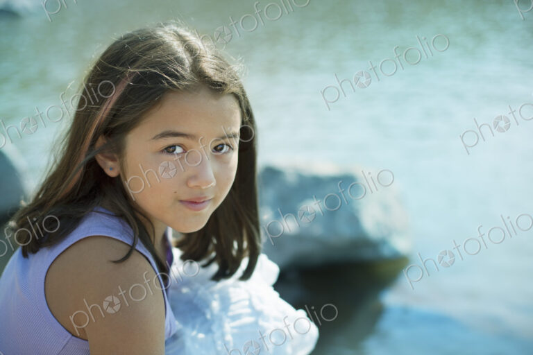 A young girl with long dark hair on the lake shore.