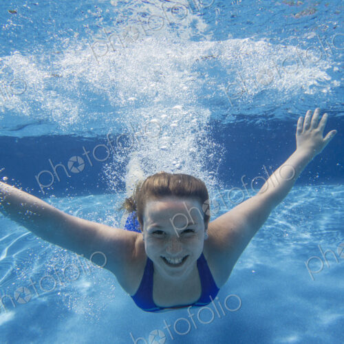 A young girl with long hair fanning out in the water, swimming underwater. A young girl with long hair fanning out in the water, swimming underwater.