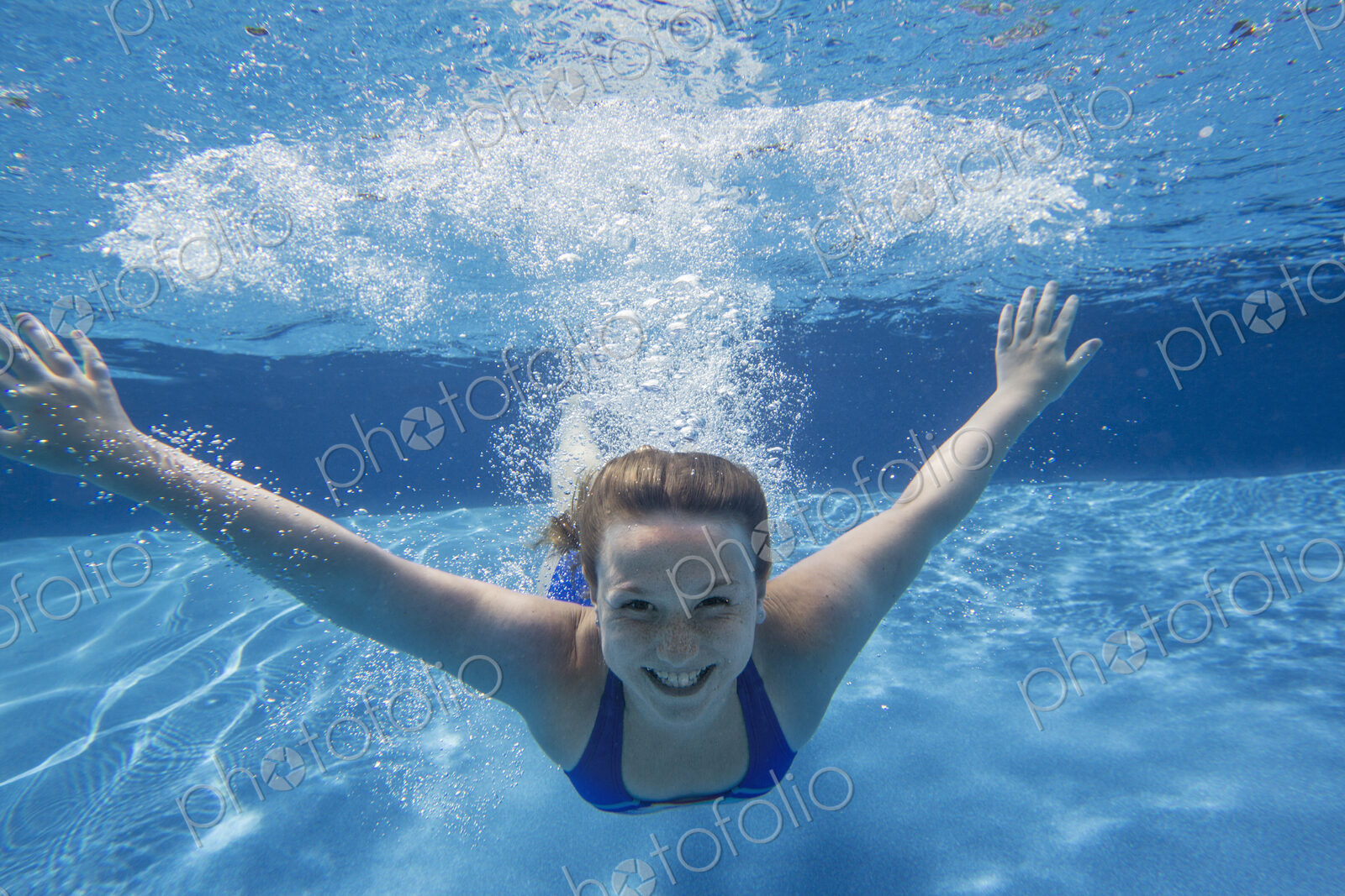 A young girl with long hair fanning out in the water, swimming underwater.
