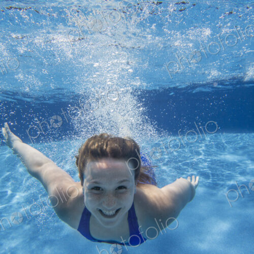 A young girl with long hair fanning out in the water, swimming underwater. A young girl with long hair fanning out in the water, swimming underwater.