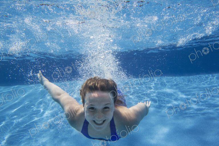 A young girl with long hair fanning out in the water, swimming underwater.
