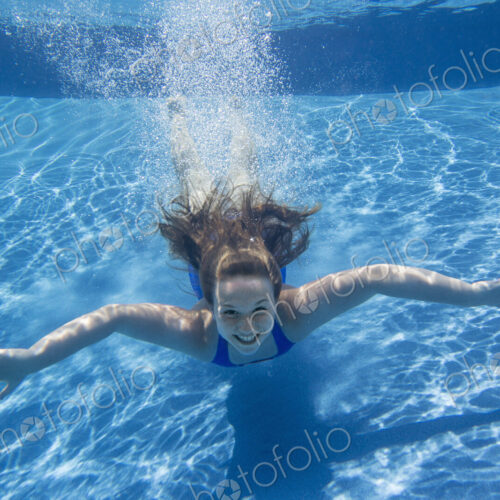 A young girl with long hair fanning out in the water, swimming underwater. A young girl with long hair fanning out in the water, swimming underwater.