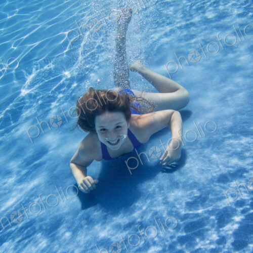 A young girl with long hair fanning out in the water, swimming underwater. A young girl with long hair fanning out in the water, swimming underwater.