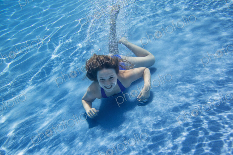 A young girl with long hair fanning out in the water, swimming underwater.