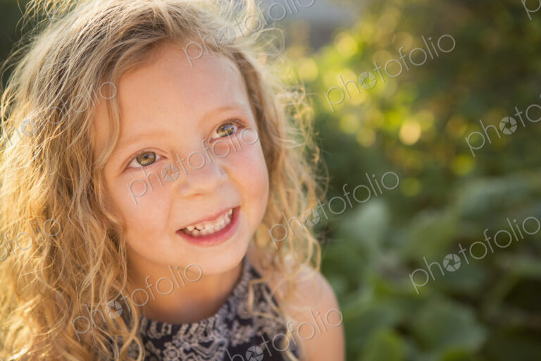 A young girl with long red curly hair outdoors in a garden.