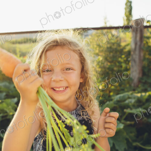 A young girl with long red curly hair outdoors in a garden holding a large fresh…