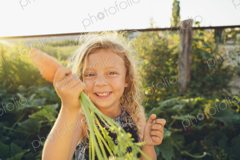 A young girl with long red curly hair outdoors in a garden holding a large fresh…