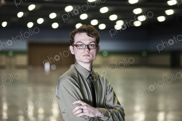 A young hip businessman standing in a dimly lit and dark exhibition area in a…